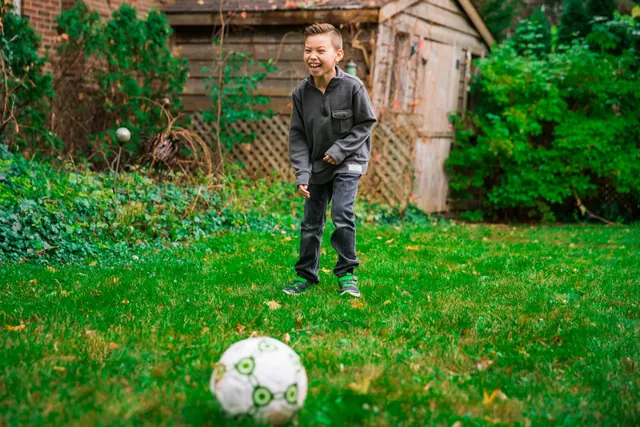 A boy laughing while playing with a football on grass