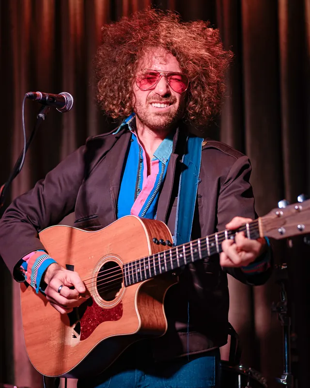 A singer playing an acoustic guitar at a microphone.