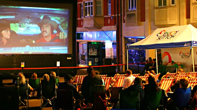 Audience seated in deckchairs watching an outdoor film screening at night.