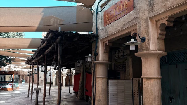 Shaded market walkway in Dubai with wooden posts and traditional-style buildings.