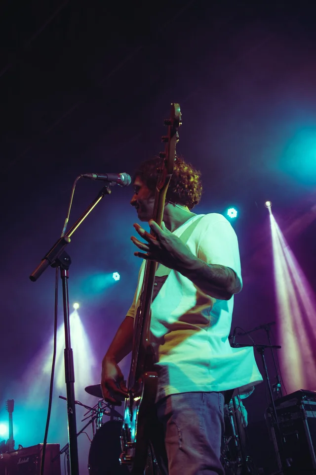 A musician plays bass guitar on a stage illuminated by blue and purple lights.
