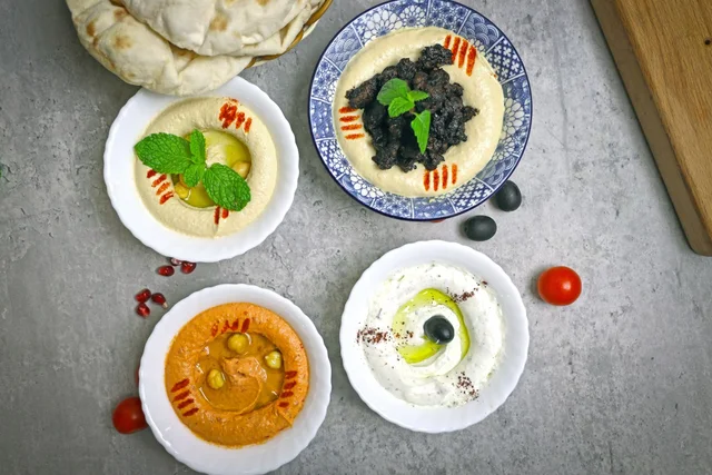 Bowls of Middle Eastern dips, including labneh and hummus, with flatbread and olives.
