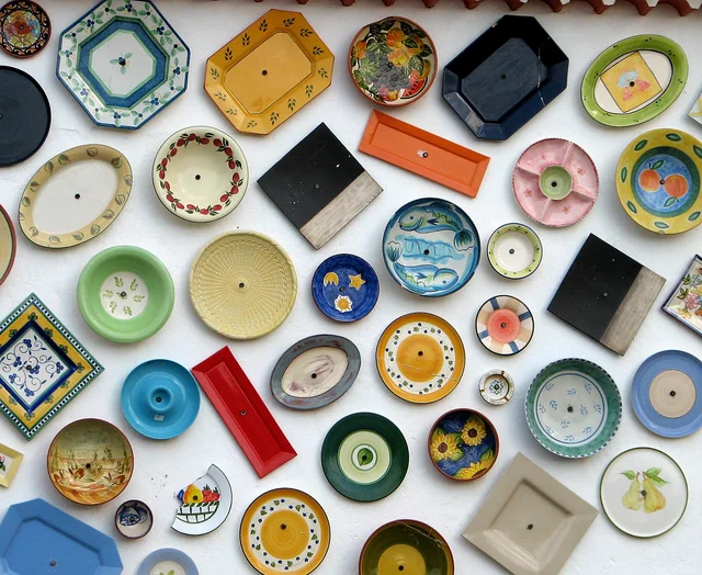 A colourful arrangement of decorated ceramic plates and serving dishes on a wall.