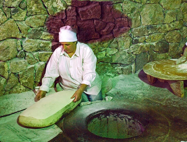A baker shapes lavash beside a traditional oven in Armenia.