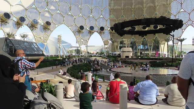 Visitors sit beneath the circular framework of Al Wasl Plaza around a central stage.