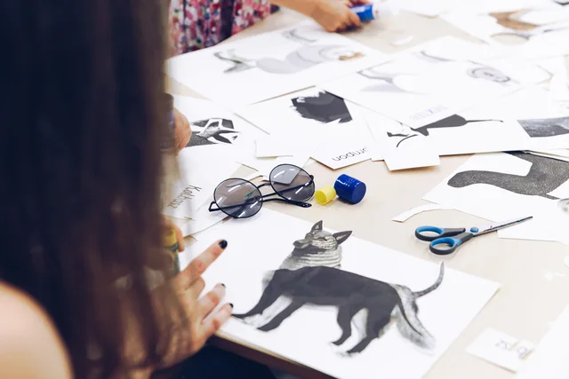 A workshop table with paper cut-outs, scissors, glue and a collage in progress.