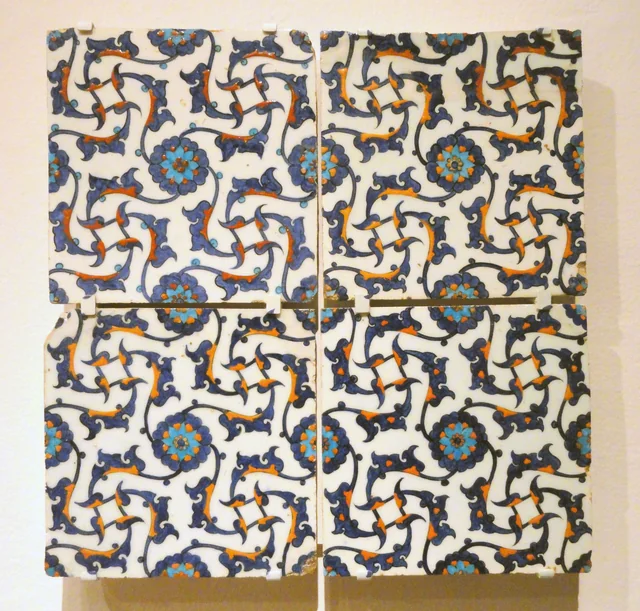 Four historic Iznik tiles with interlocking blue and orange ornamental motifs.