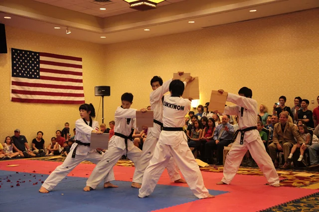 Kukkiwon taekwondo performers demonstrating board-breaking in front of an audience.