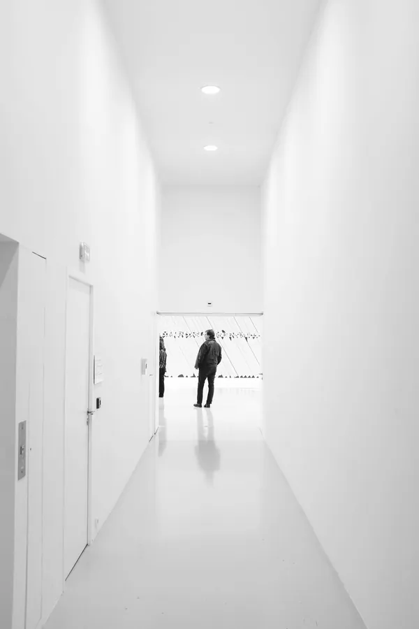 A bright white gallery corridor with framed art and distant visitors.