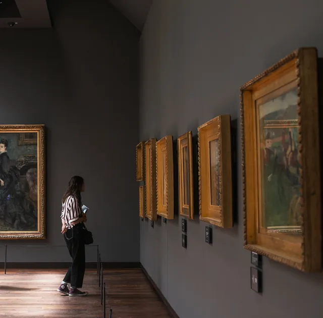 A visitor walking past paintings in an art gallery.