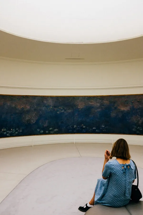 A visitor sitting quietly in front of a large gallery painting.